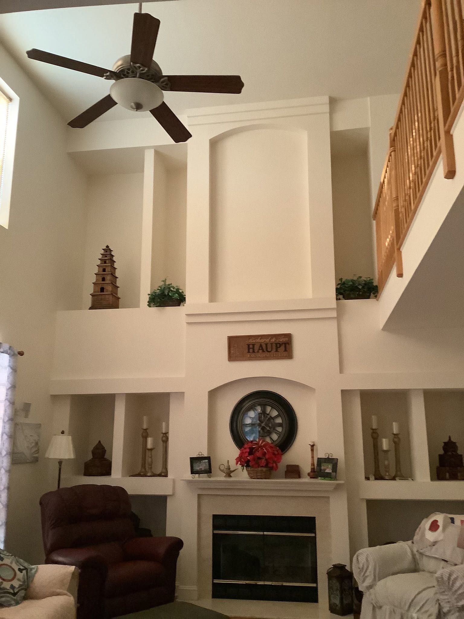 Living room with a fireplace, tall white walls, ceiling fan, staircase, and burgundy recliner chairs