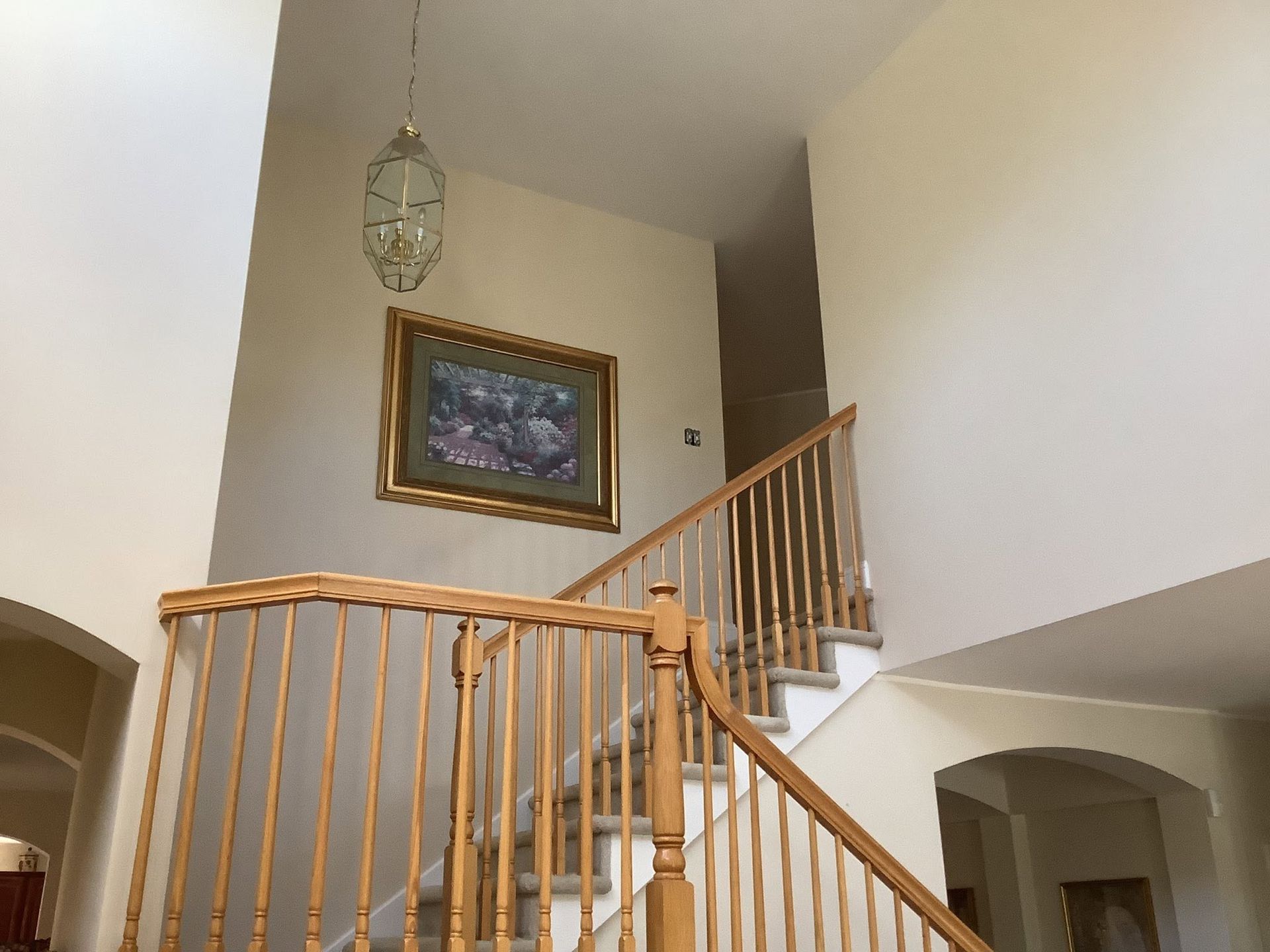 Wooden staircase with curved railing in a bright foyer, framed painting on the wall above.
