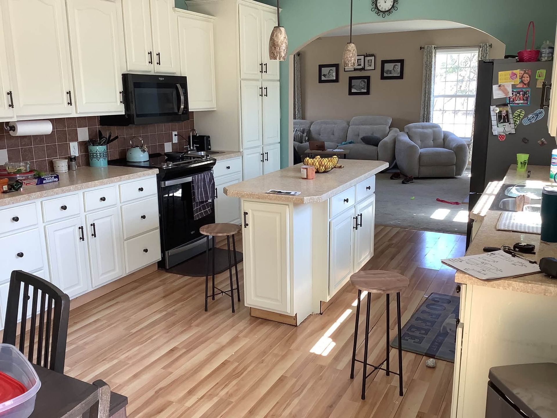 Bright kitchen with white cabinets, central island, and view into a cozy living room with gray sofa.