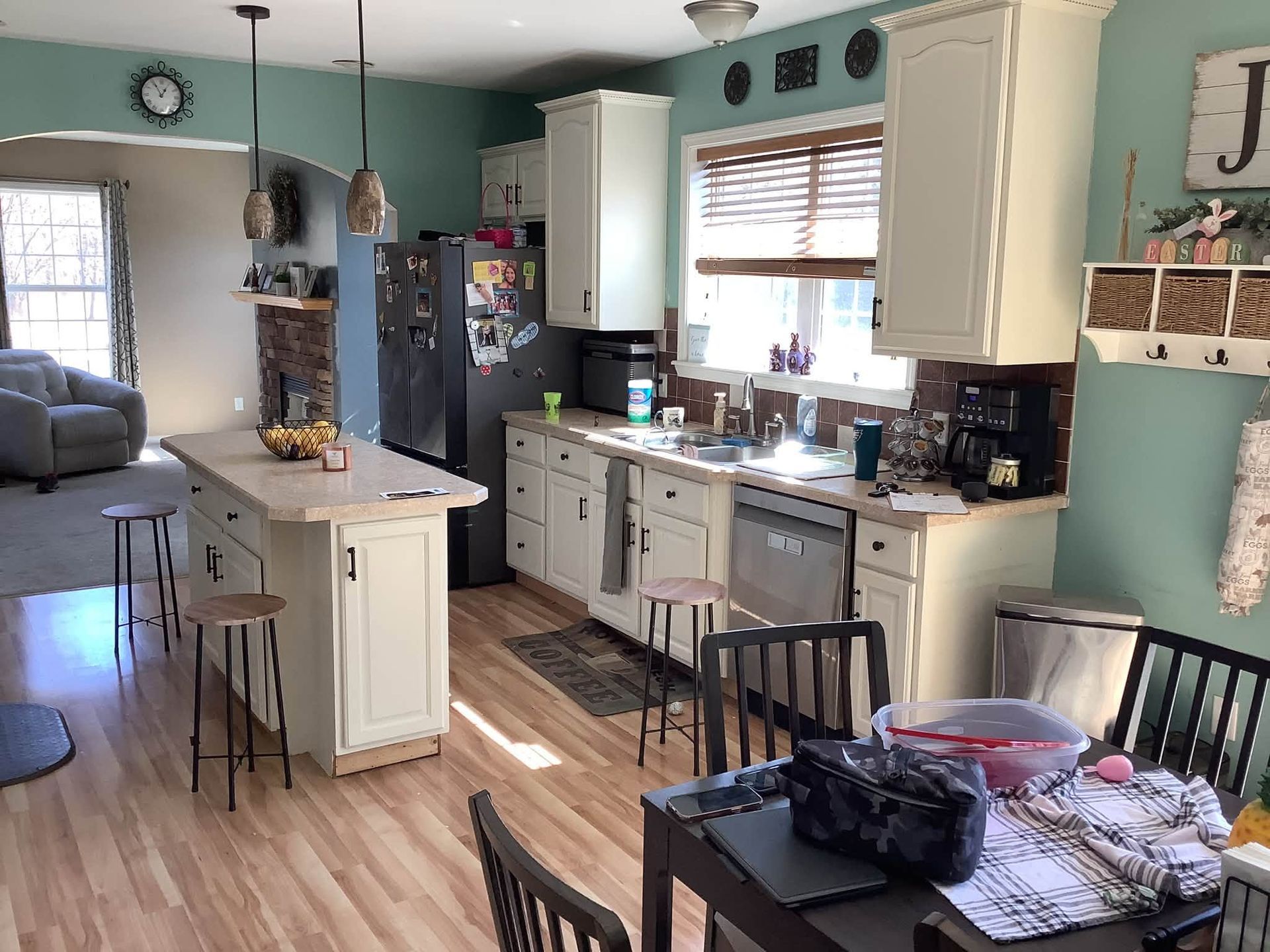 Bright kitchen with teal walls, white cabinets, island, black fridge, and dining table in the foreground