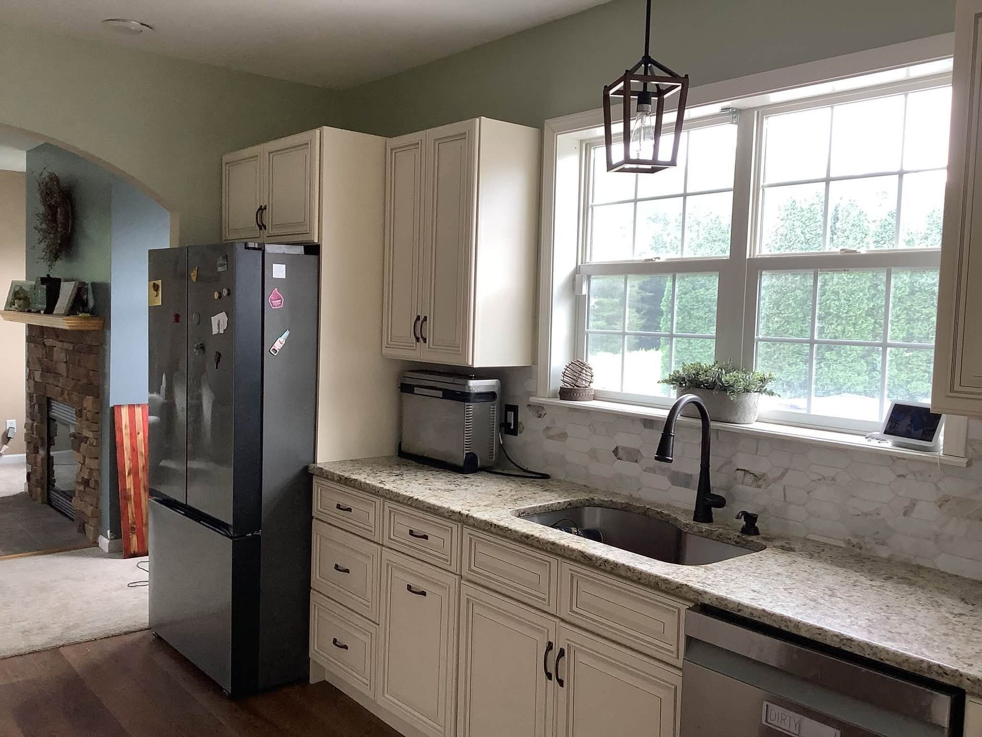 Bright kitchen with white cabinets, black refrigerator, and large window over the sink.