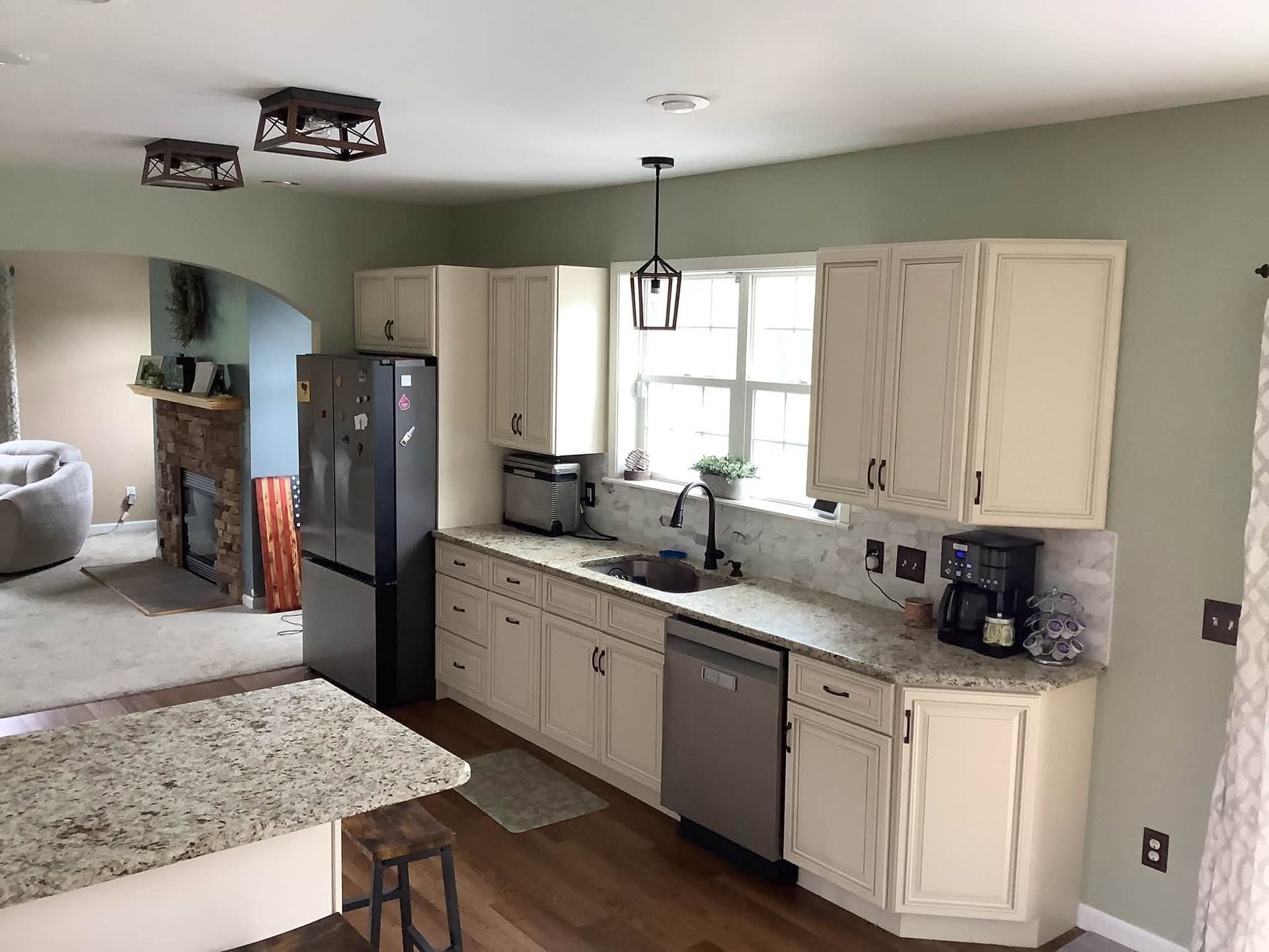 Bright kitchen with white cabinets, black appliances, granite counters, and an arched doorway to a living room
