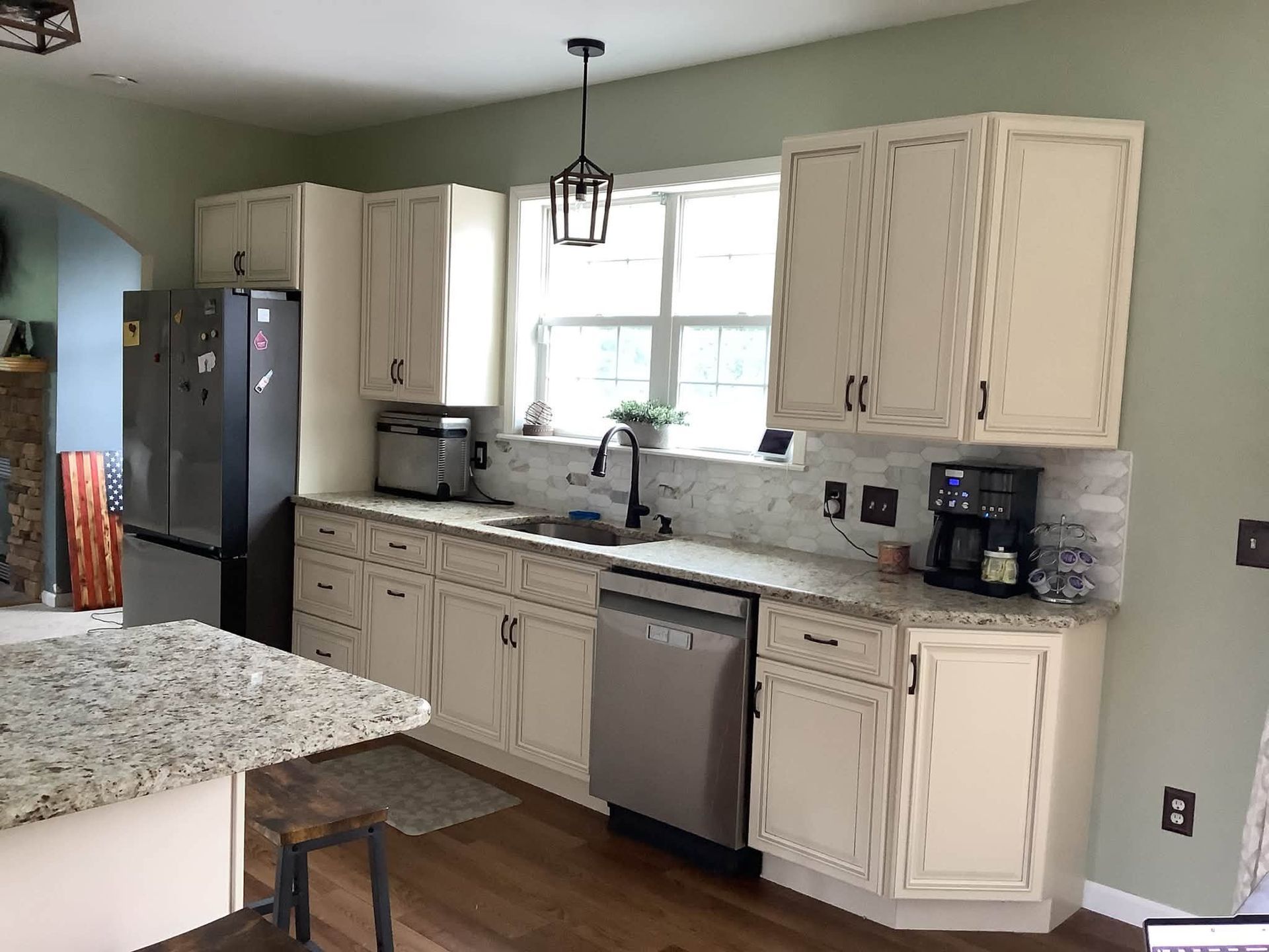 Bright kitchen with cream cabinets, granite island, stainless dishwasher, and black refrigerator by a window