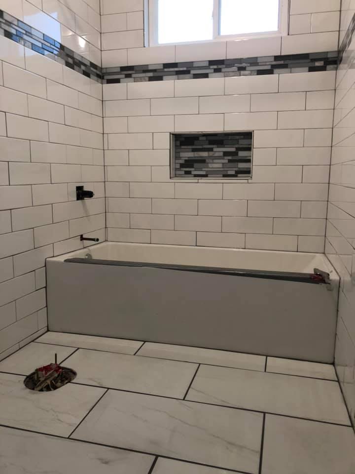 A bathroom with white tiles and a bathtub.