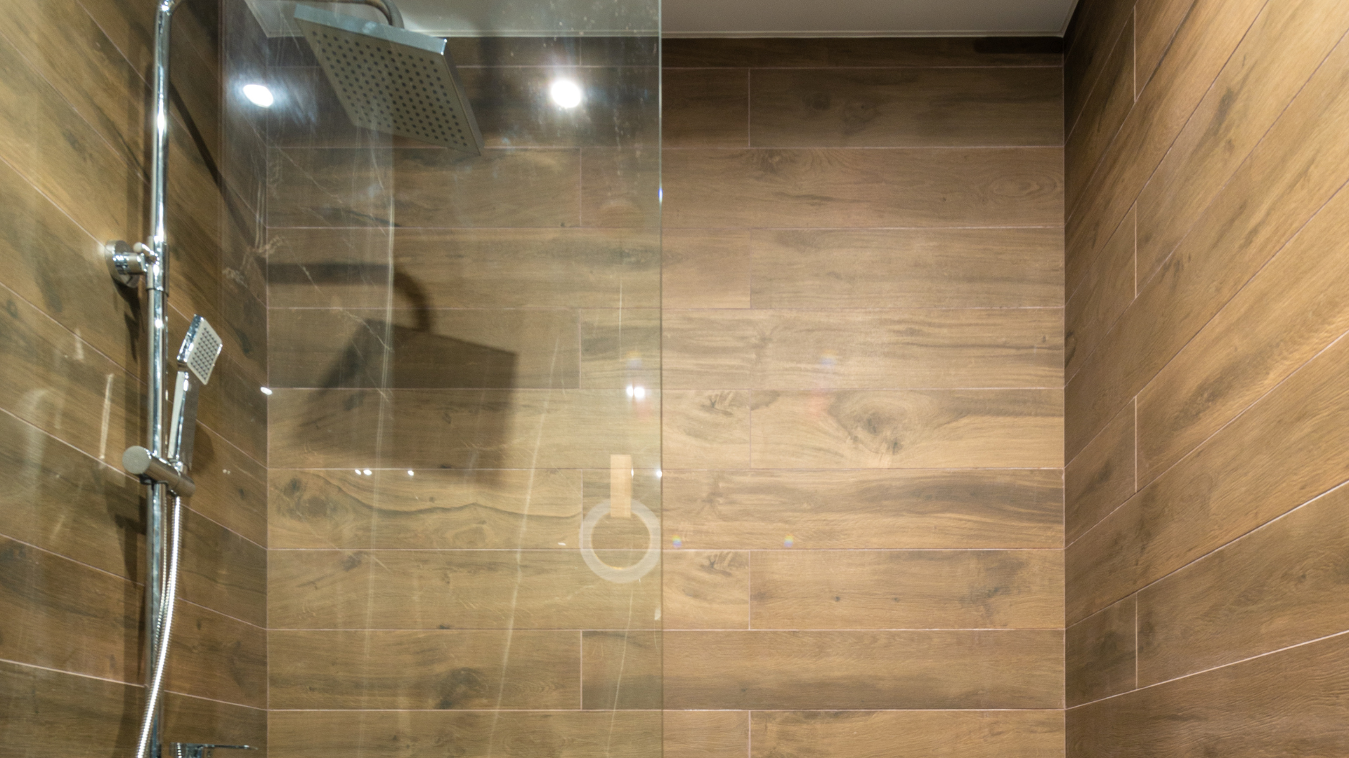 A bathroom with wooden tiles and a walk in shower with a glass door.