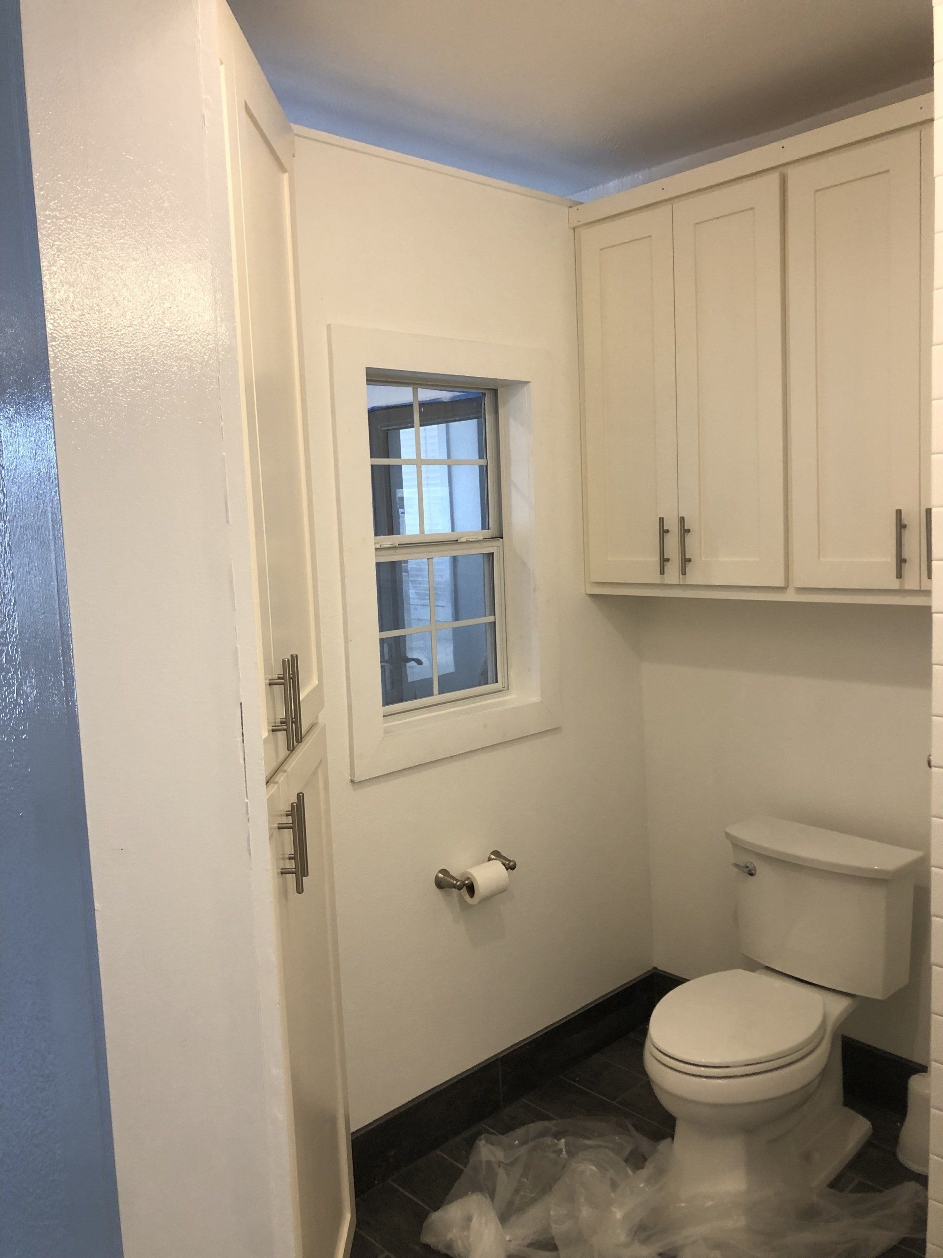 A bathroom with a toilet , cabinets , and a window.
