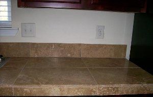 A kitchen counter with a tile counter top and a window.