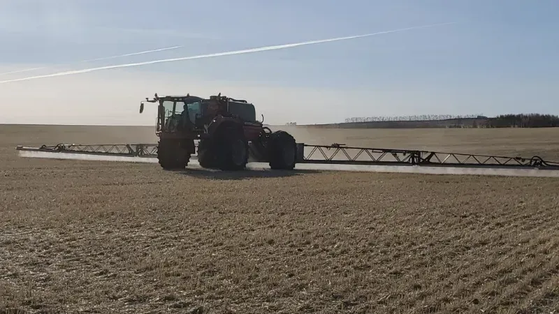 A tractor is spraying a field with a sprayer.