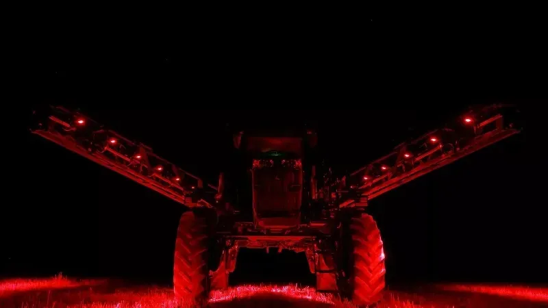 A tractor with red lights on it is spraying a field at night.