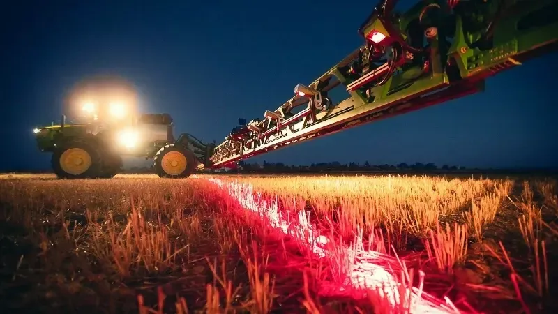 A tractor is spraying a field with a red LED coming out of it