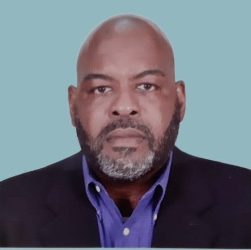 A bald man with a beard is wearing a suit and a blue shirt.