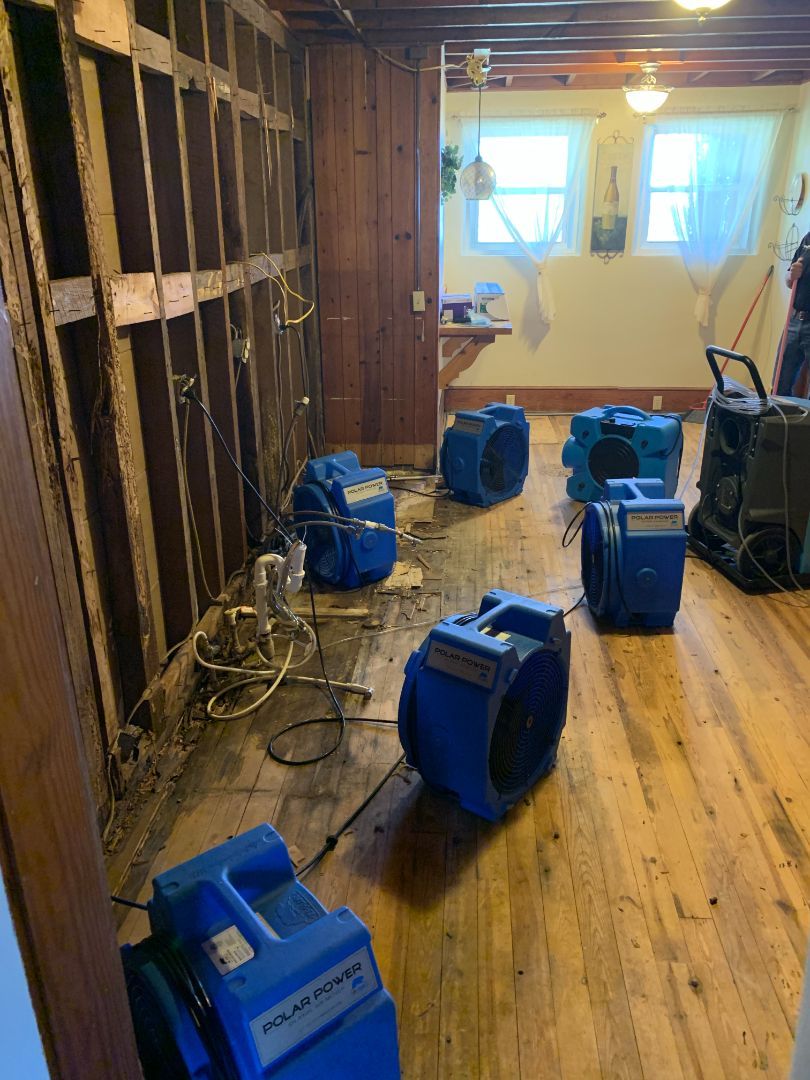 Basement undergoing water damage remediation; fans drying wooden floors and exposed wall studs.