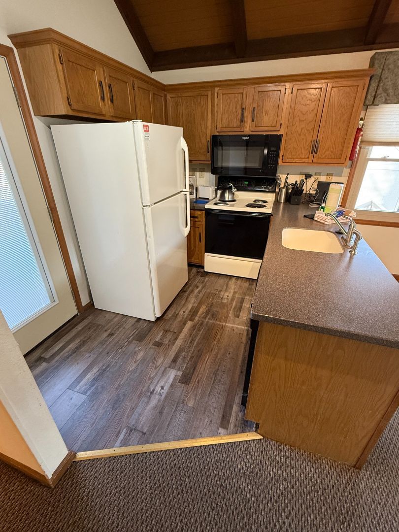 Kitchen with wood cabinets, white fridge, black stove, brown countertop, and wood-look flooring.