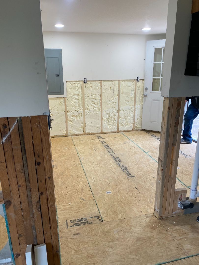 Partially renovated room with exposed insulation, plywood floor, and open wall framing