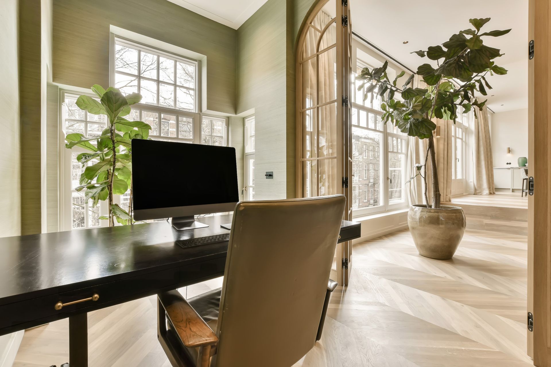 Office with desk, computer, large windows, green walls, and potted plants.