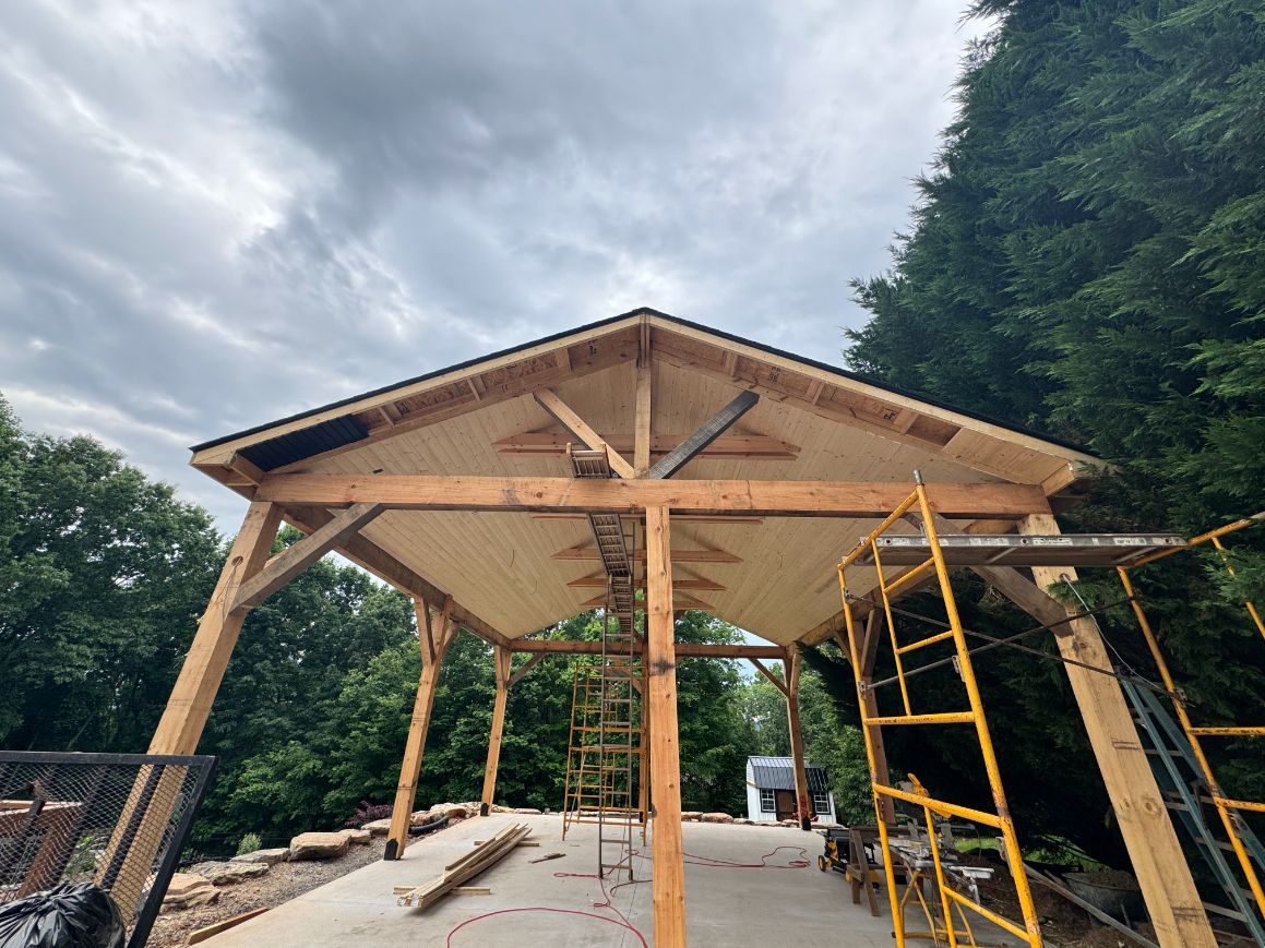 Partially built wooden pavilion with scaffolding and ladder outdoors under a cloudy sky
