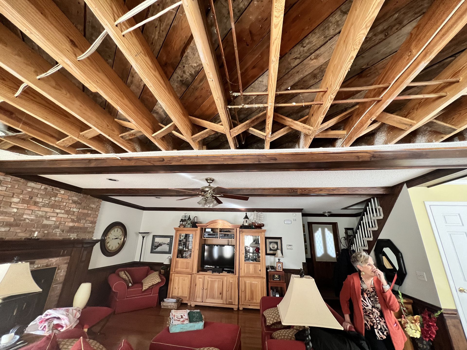 Living room with exposed ceiling beams; woman stands near door; furniture and brick wall.