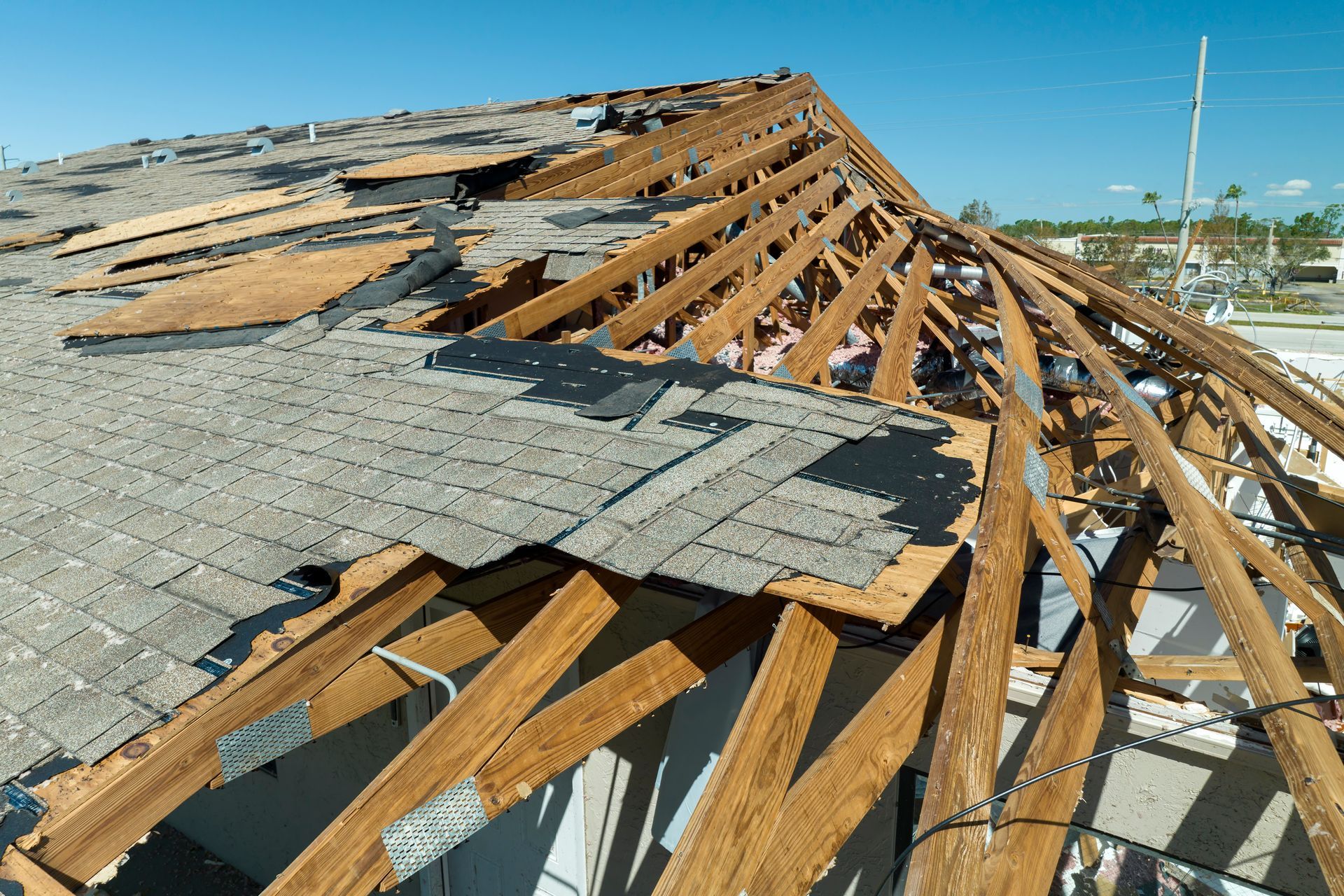 Damaged roof with missing shingles and exposed wooden beams under a clear, blue sky.