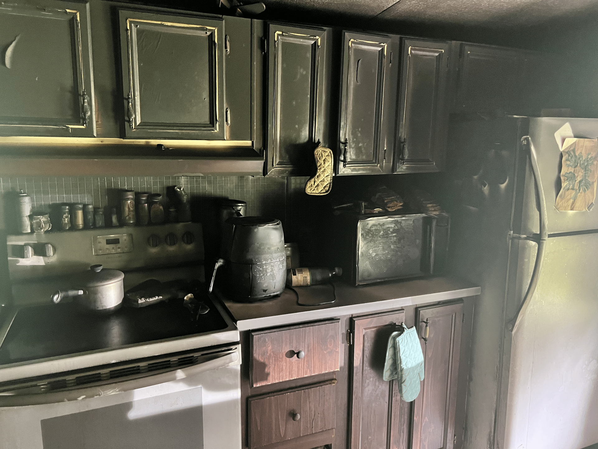 Kitchen with fire damage: black cabinets, stove, and appliances covered in soot.