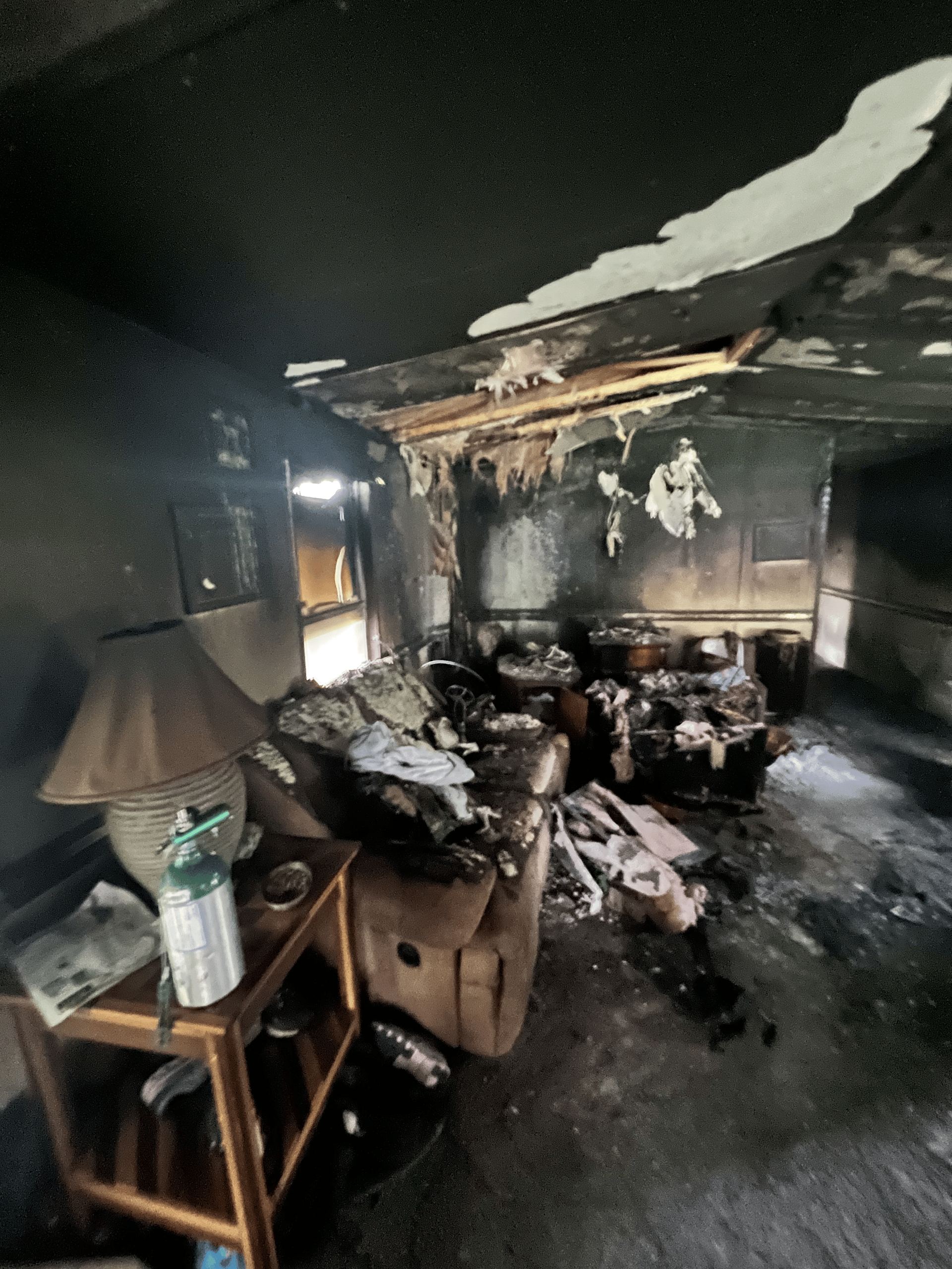 Interior of a room severely damaged by fire, walls and ceiling blackened, furniture charred.