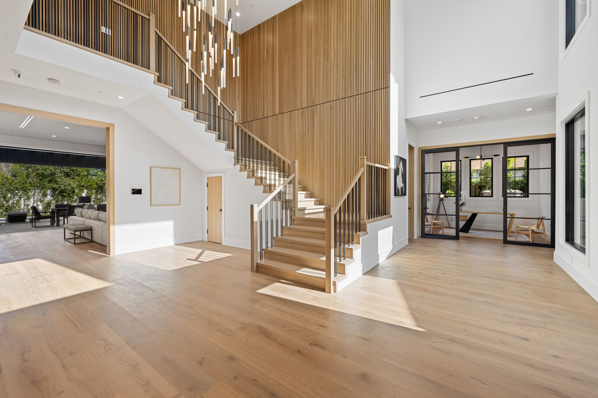 Spacious entryway with wooden staircase and light wood flooring, leading to multiple rooms with natural light.