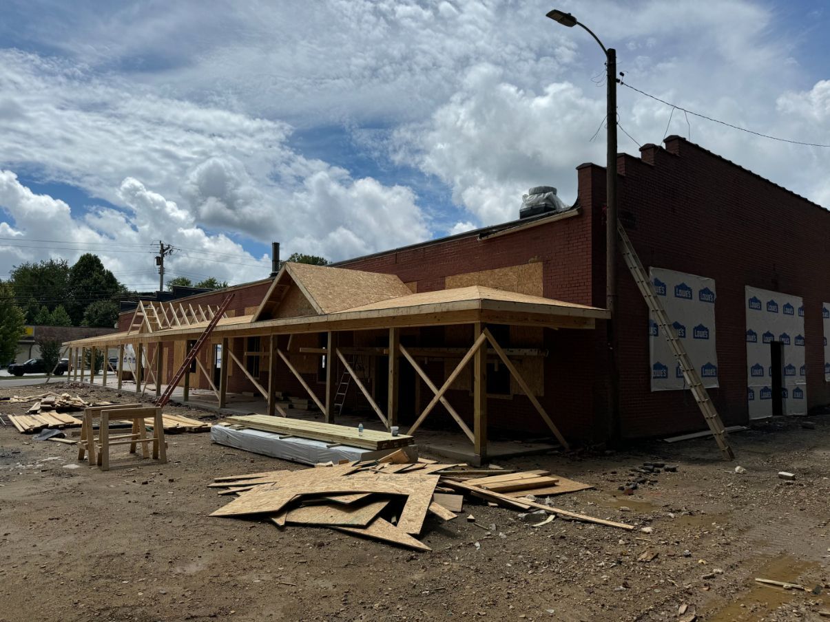 Damaged storefront with exposed wooden support beams and debris scattered outside under a cloudy sky