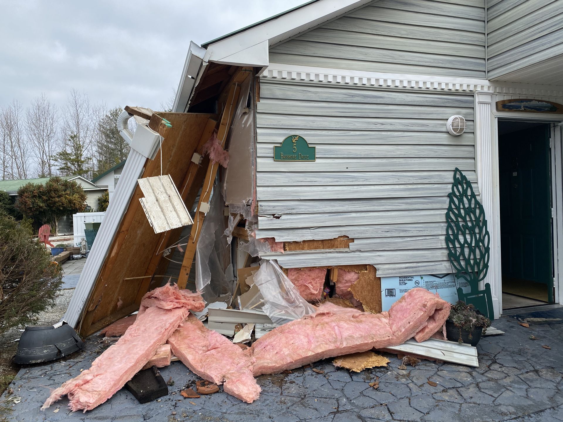 Damaged house facade with exposed insulation and structural damage; exterior daylight.