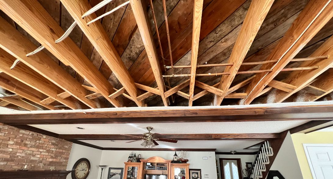 Exposed wooden ceiling beams above a living room with a ceiling fan and framed wall decor