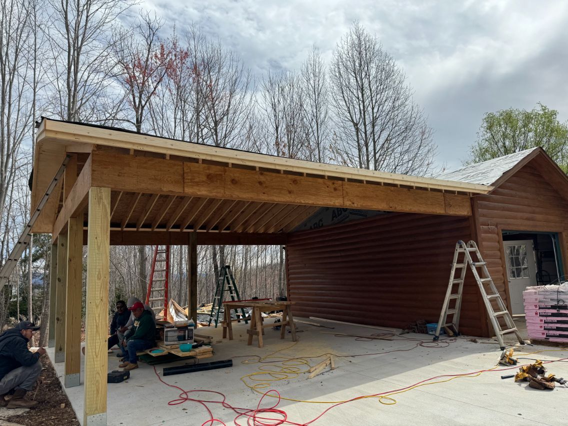Wooden carport under roof construction beside a cabin, with ladders, tools, and workers.