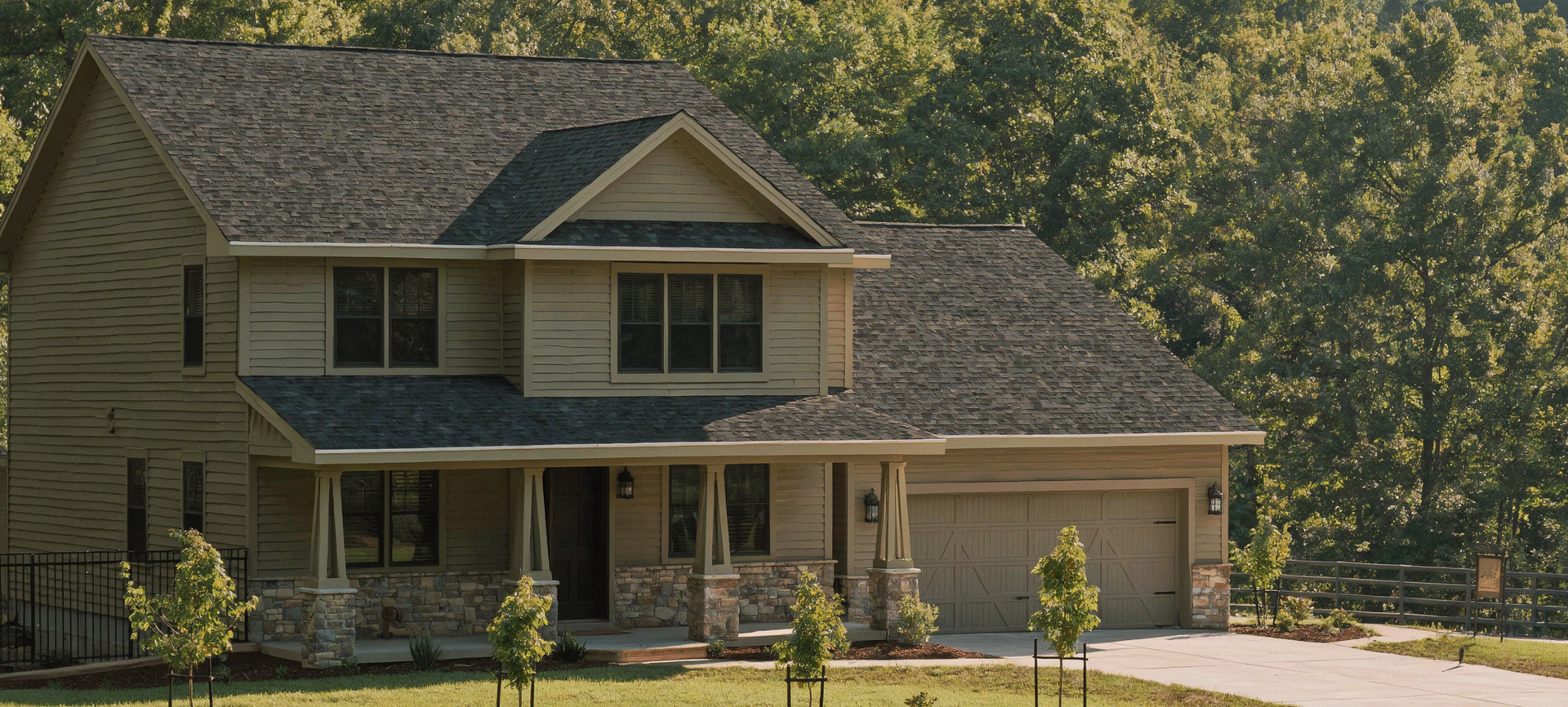 Two-story gray custom house with front porch, driveway, and trees in the background