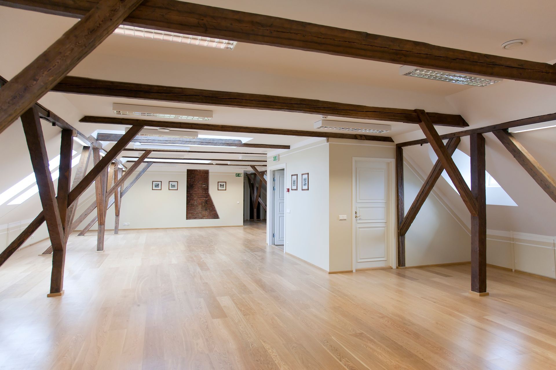 Bright, empty room with wooden beams and a light wood floor. Features white walls, a doorway, and recessed lighting.