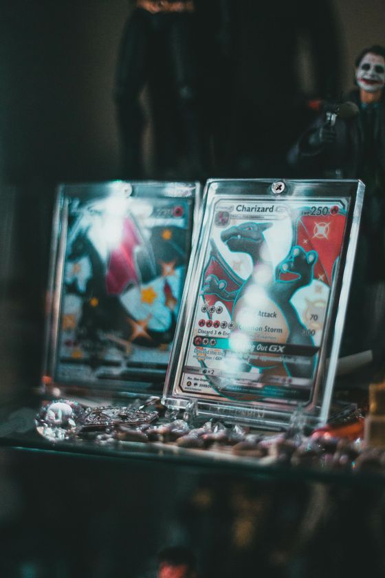 Two collectible cards displayed on a dark table with red and teal artwork, one featuring a white cat-like figure.
