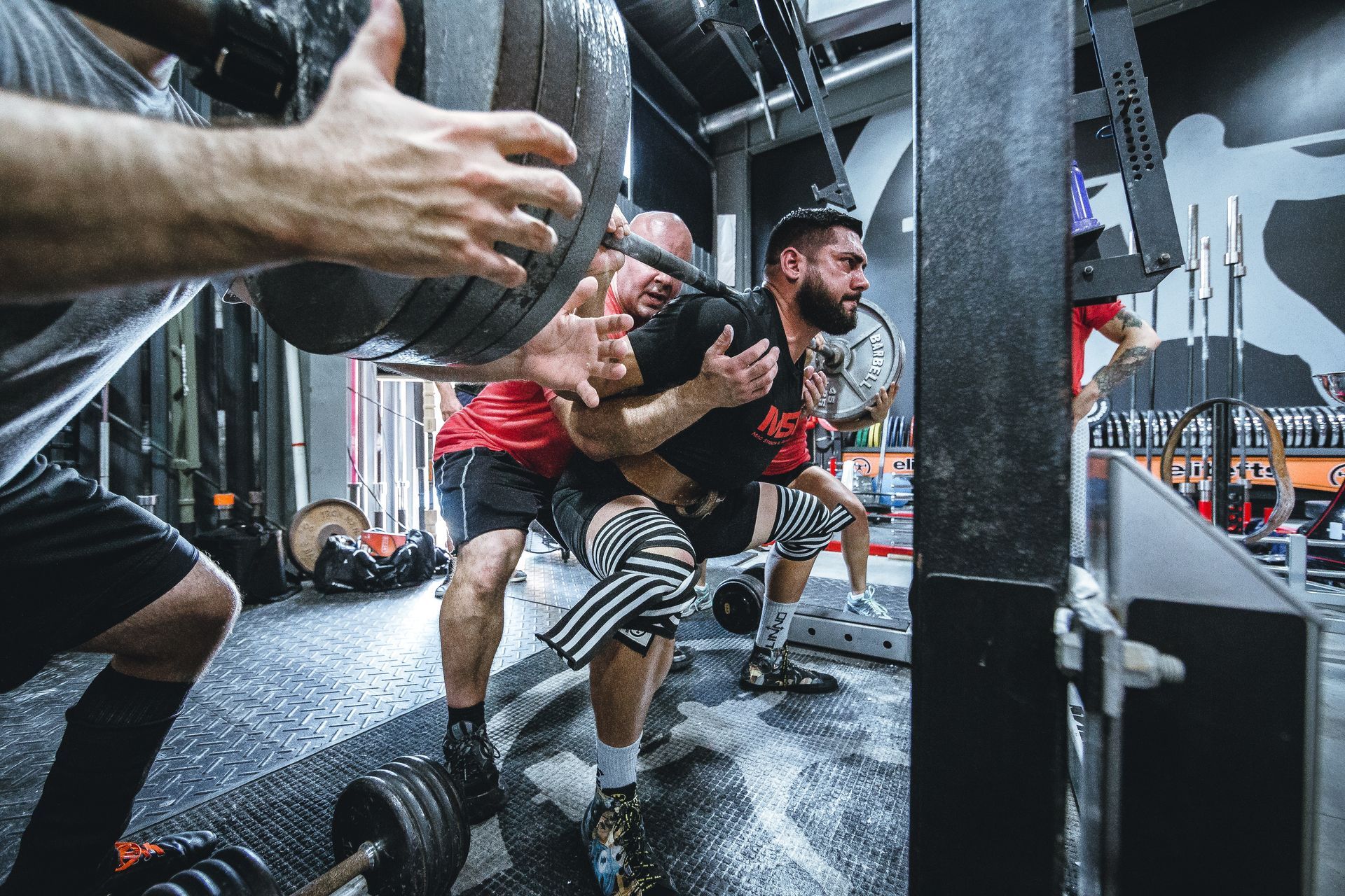 A group of men are squatting with dumbbells in a gym.