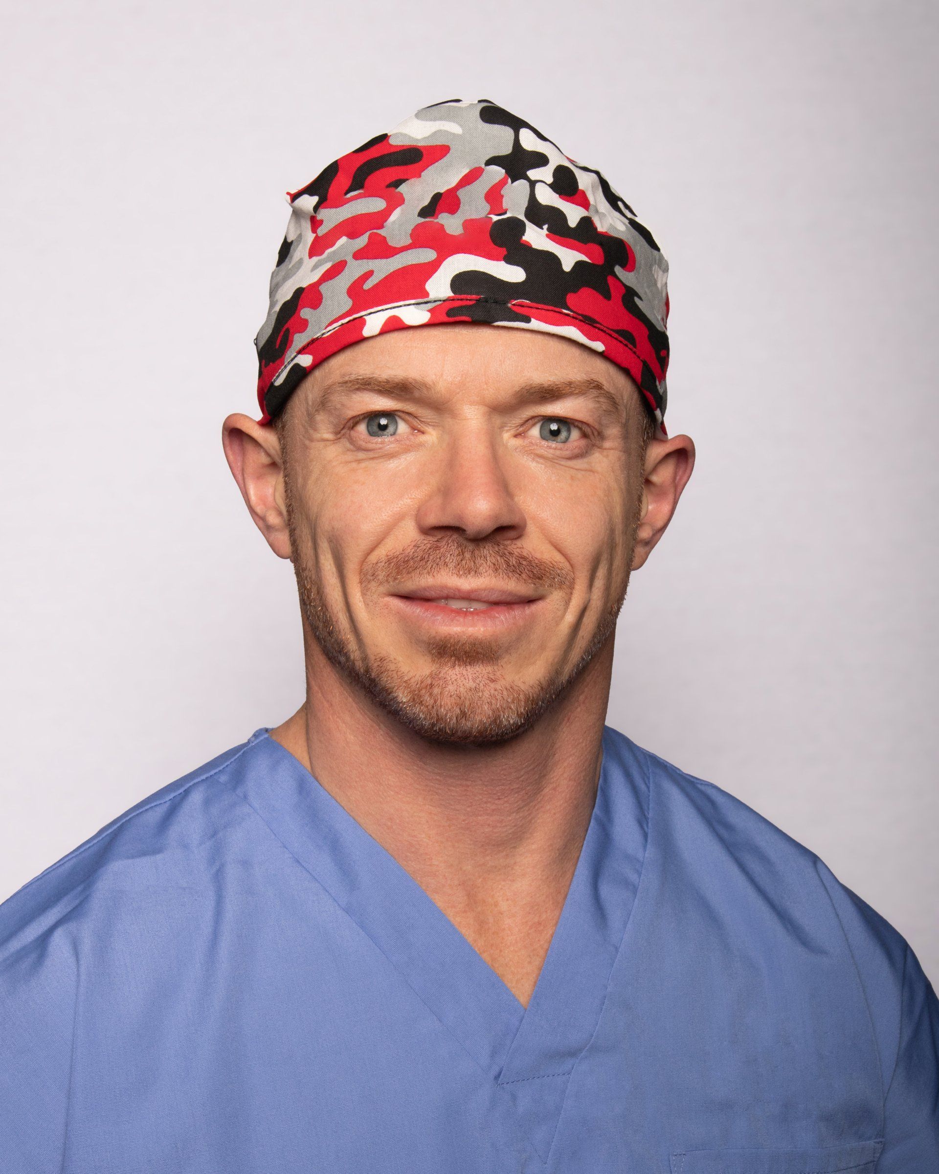 Dr Owen Wall wearing a hat and scrubs is smiling for the camera.