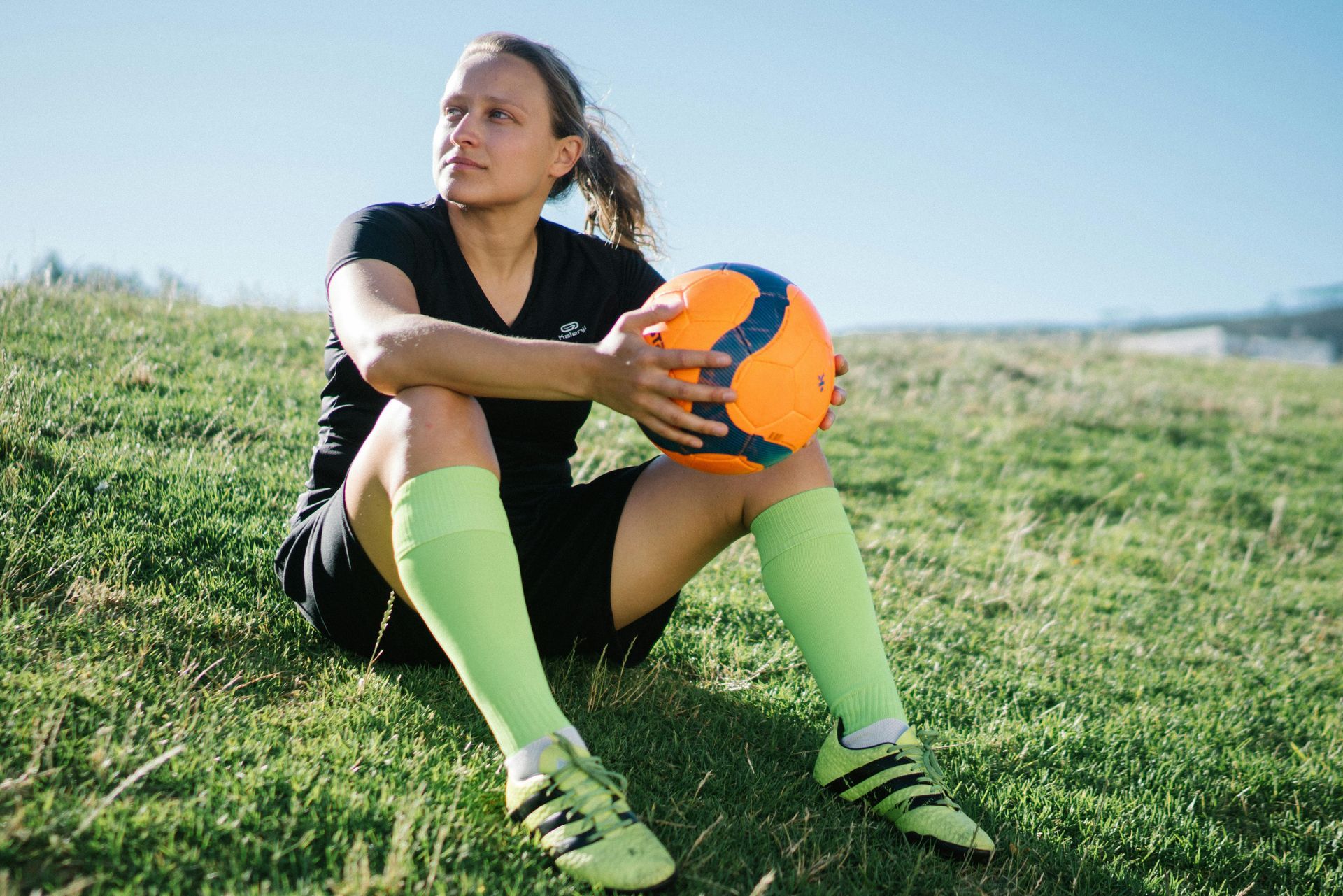 female footballer sits down on grass holding a football