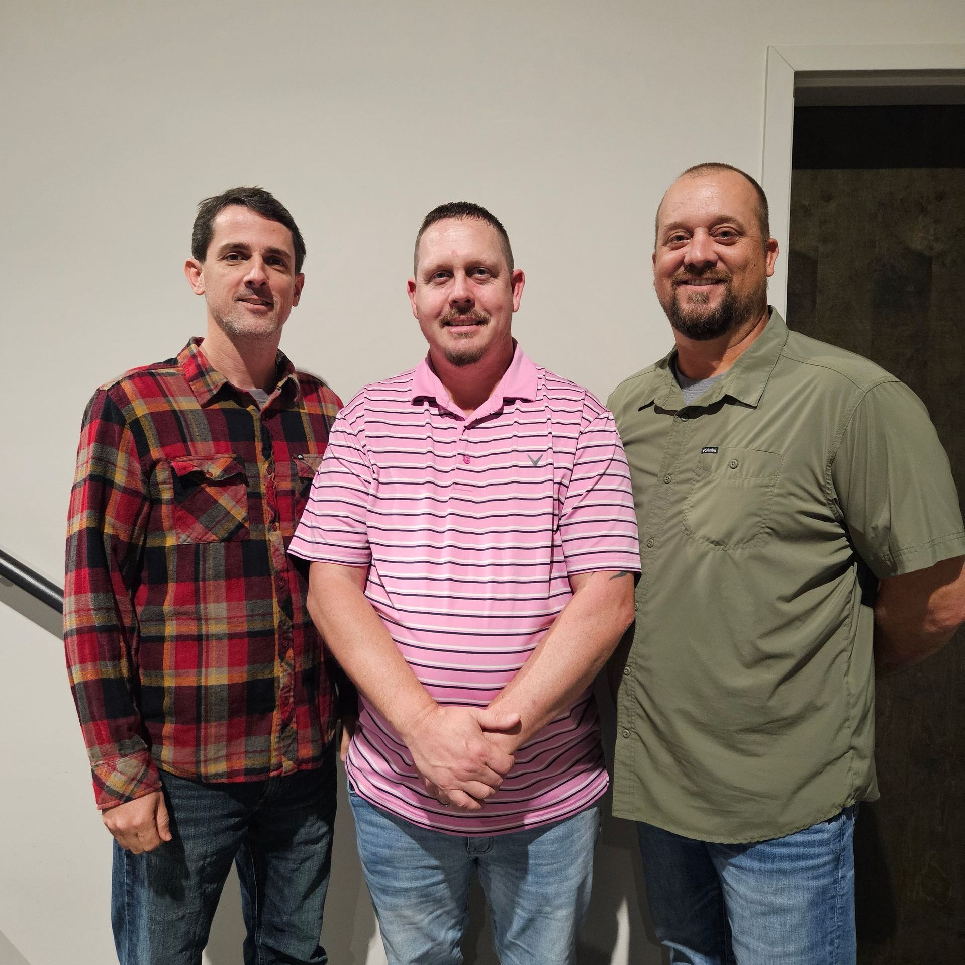 Three men are posing for a picture and one of them is wearing a pink shirt