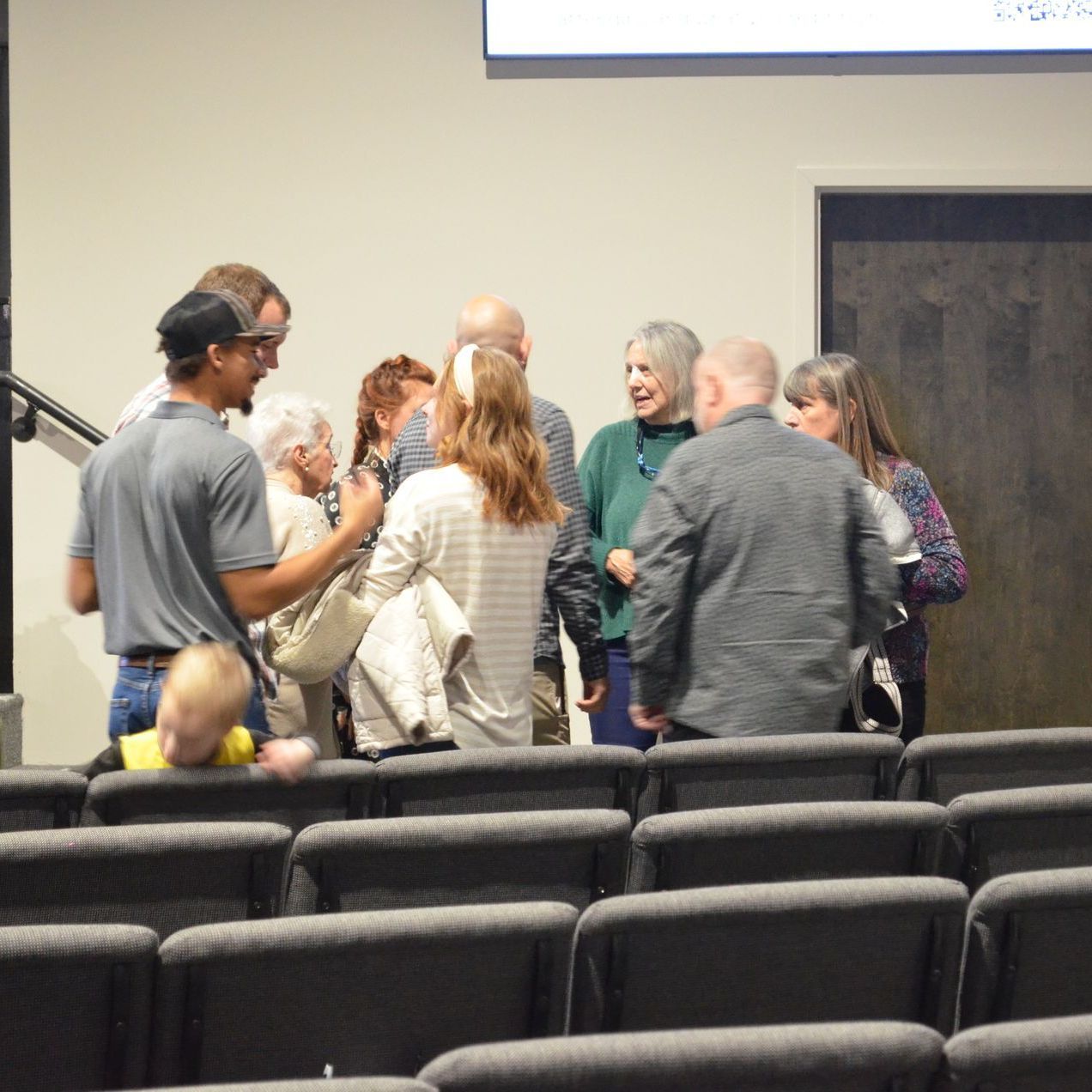 A group of people are standing in an auditorium talking to each other