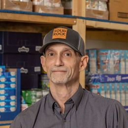 A man wearing a hat is standing in front of a shelf in a store.