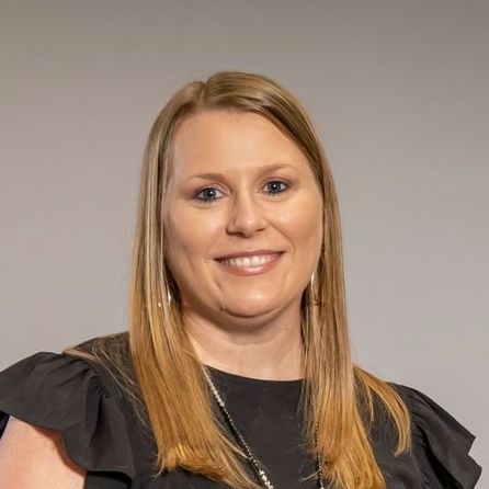 A woman with long blonde hair is wearing a black shirt and smiling.