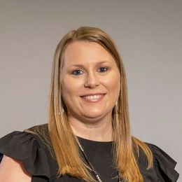 A woman with long blonde hair is wearing a black shirt and smiling.