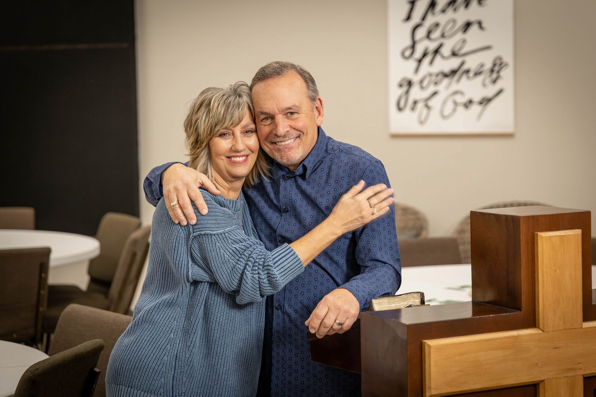 A man and a woman are posing for a picture in front of a cross in a church.