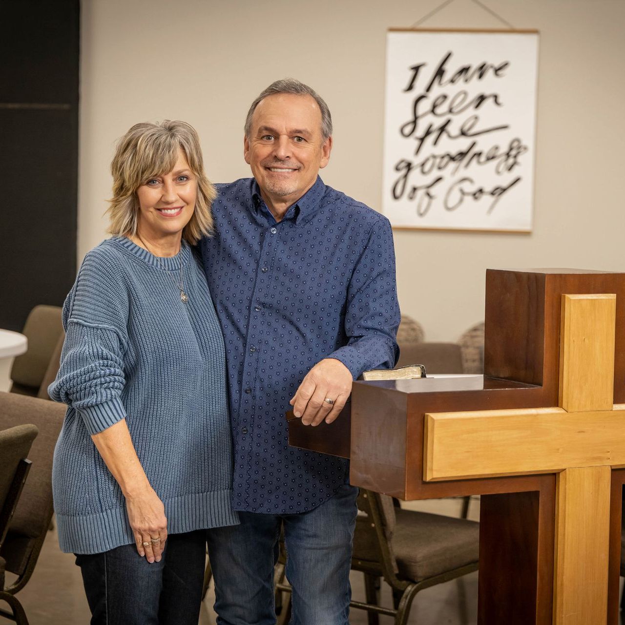 A man and a woman are posing for a picture in front of a cross.