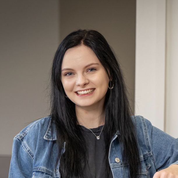 A woman wearing a denim jacket and a black shirt is smiling for the camera.