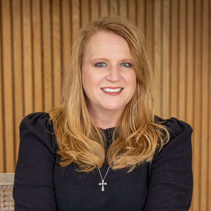A woman wearing a black sweater and a cross necklace is smiling for the camera.