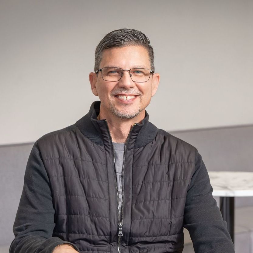 A man wearing glasses and a black jacket is smiling for the camera.
