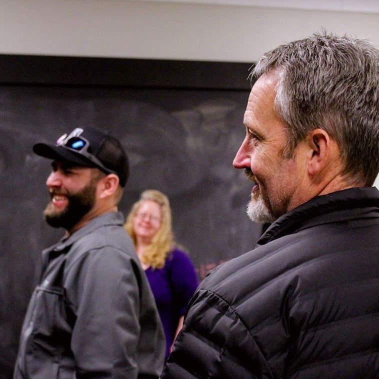 Two men are standing next to each other in front of a blackboard