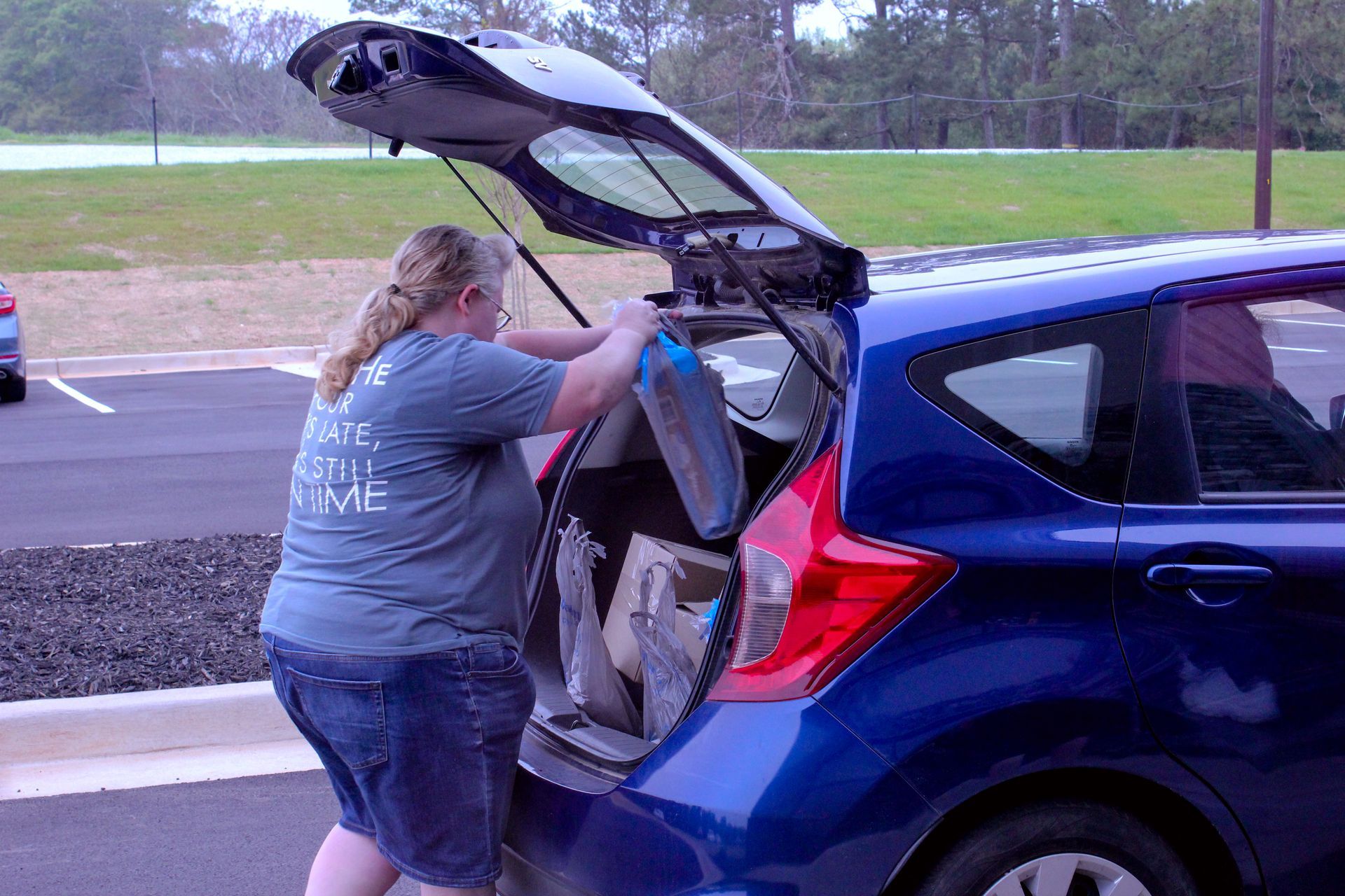 A woman is putting something in the back of a blue car.