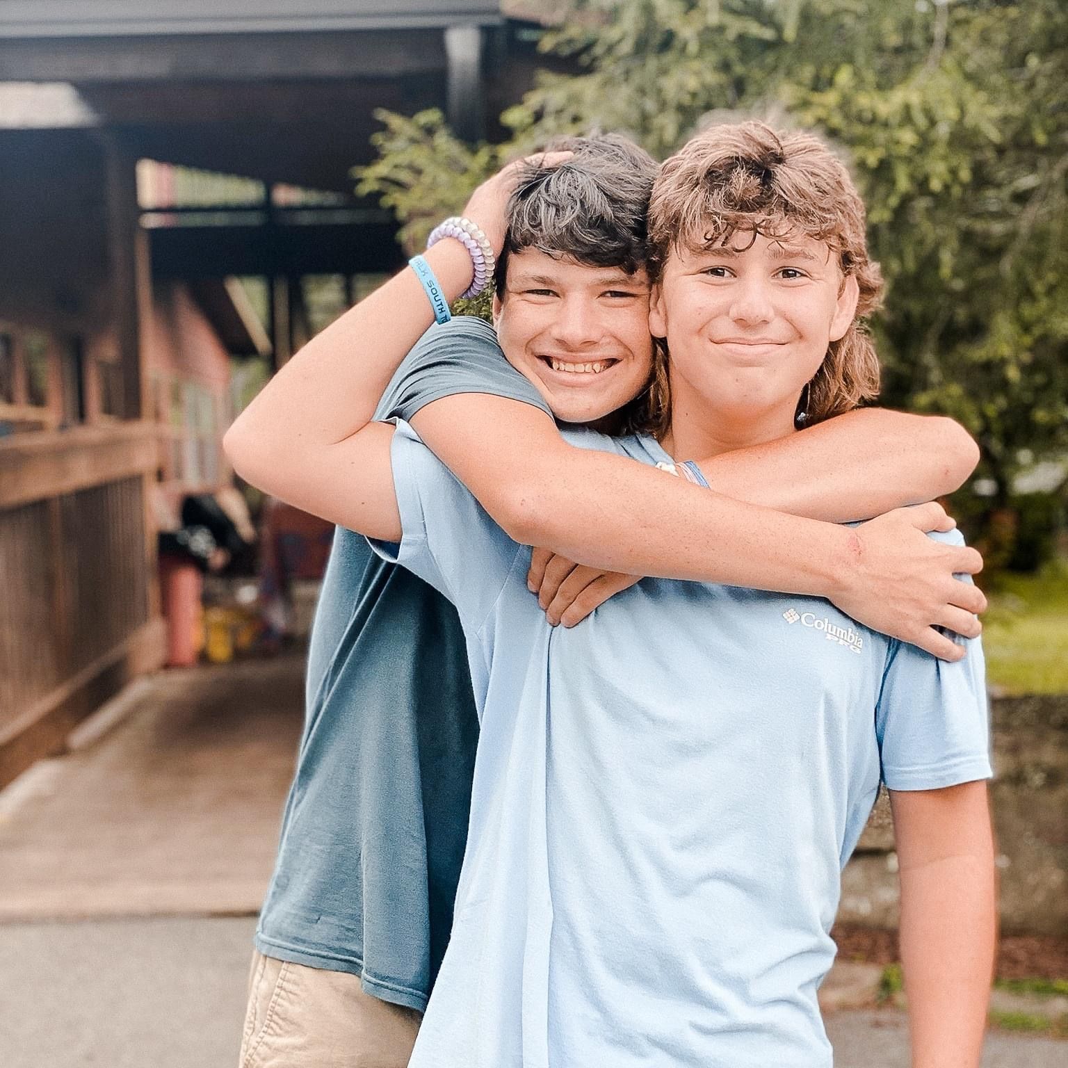 Two young boys are hugging each other in front of a house.