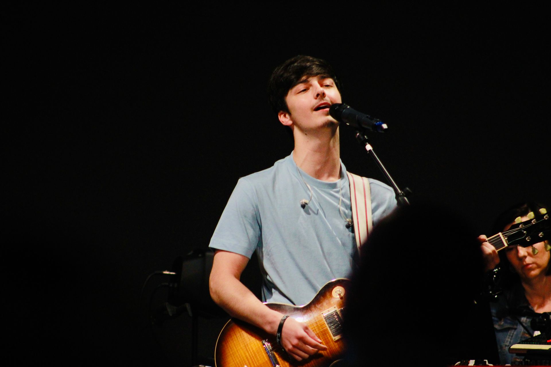 A man is singing into a microphone while holding a guitar.