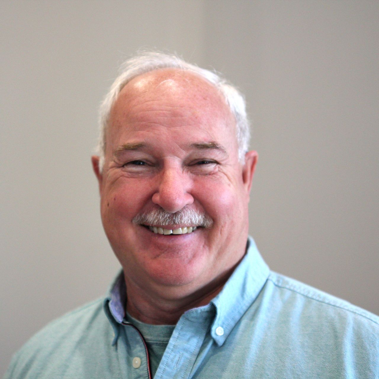 A man with a mustache is smiling for the camera while wearing a blue shirt.